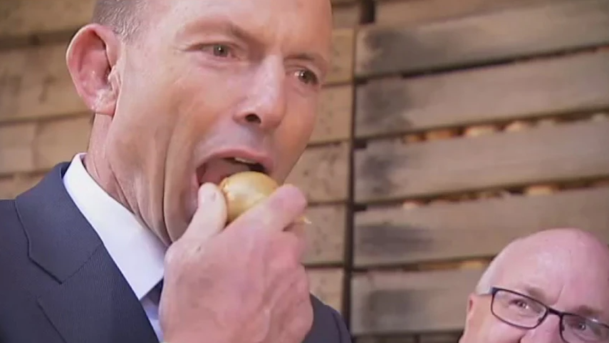 Tony Abbott biting into a raw onion